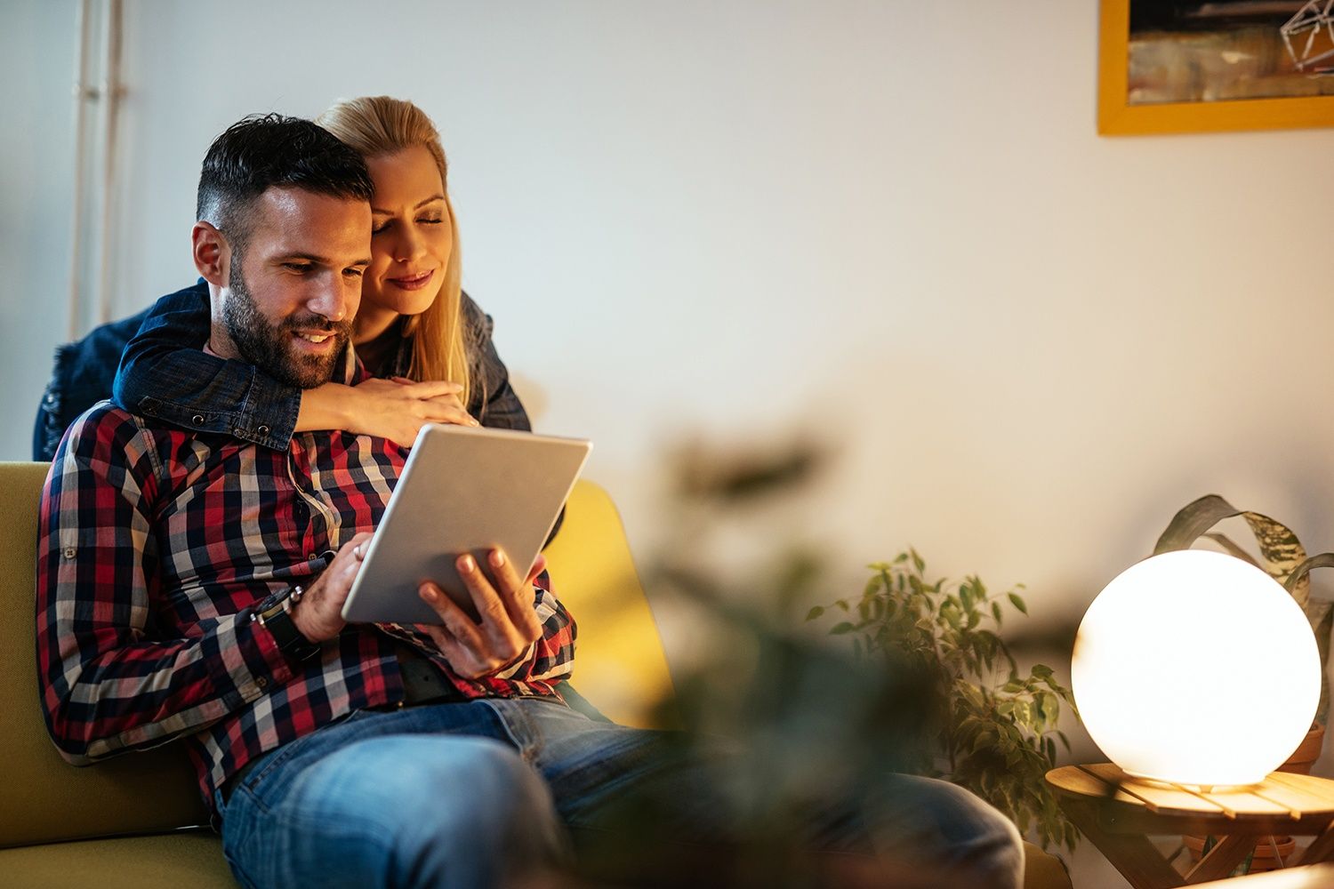 Paar sitzt gemütlich auf der Couch und liest in einem Tablet